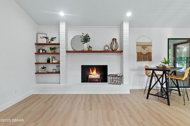 living room with a brick fireplace, light hardwood / wood-style flooring, and brick wall