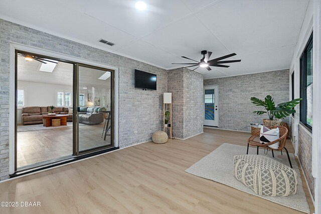 sitting room with hardwood / wood-style flooring, brick wall, ceiling fan, and a skylight