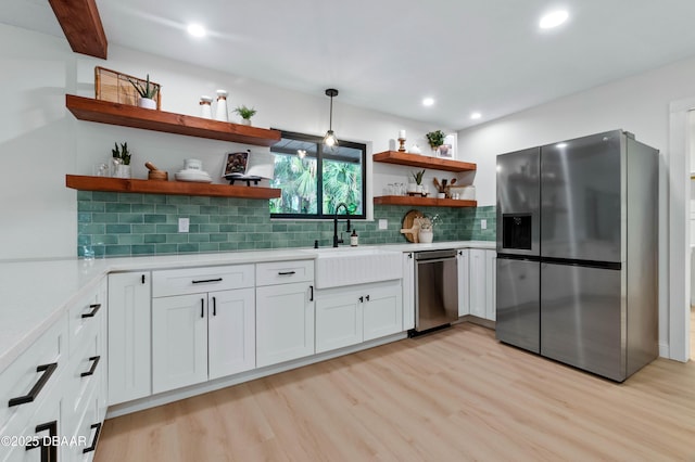 kitchen with sink, light hardwood / wood-style flooring, appliances with stainless steel finishes, pendant lighting, and white cabinets