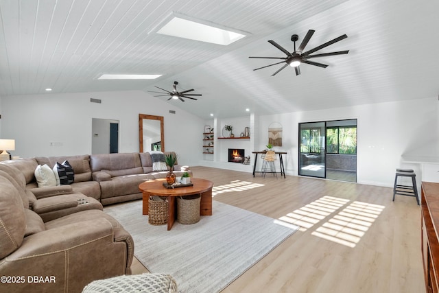 living room featuring vaulted ceiling with skylight, light hardwood / wood-style floors, a large fireplace, and ceiling fan