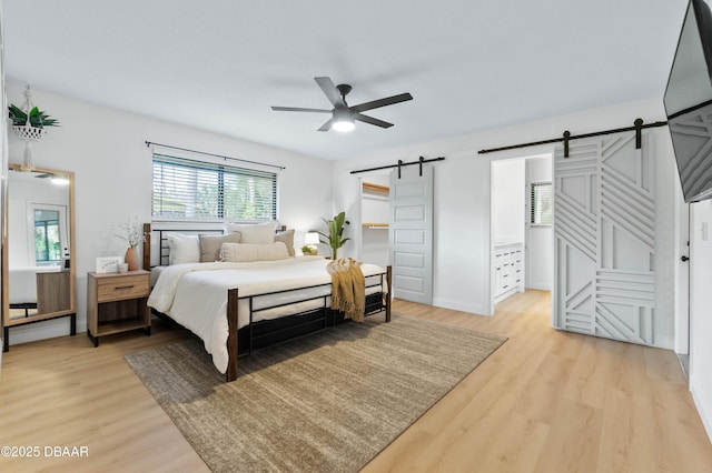 bedroom with ceiling fan, a barn door, and light hardwood / wood-style floors