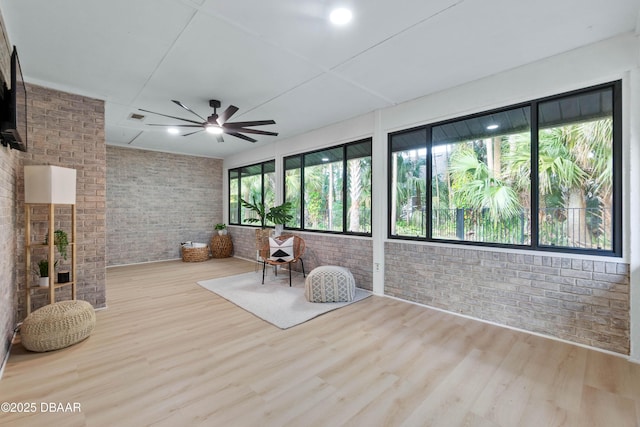 interior space with ceiling fan, brick wall, and light hardwood / wood-style floors