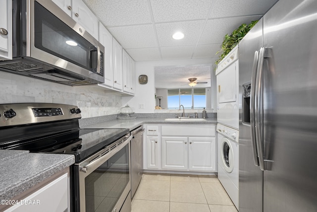 kitchen featuring stainless steel appliances, white cabinets, a paneled ceiling, sink, and stacked washer and dryer