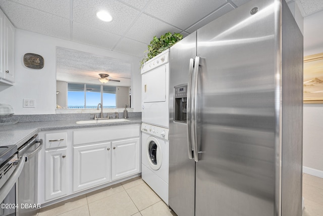 kitchen featuring white cabinets, a paneled ceiling, stacked washer / dryer, light tile patterned flooring, and appliances with stainless steel finishes