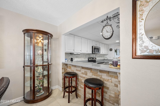 kitchen with white cabinets, decorative backsplash, a breakfast bar area, light tile patterned flooring, and appliances with stainless steel finishes