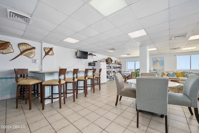 dining space with a drop ceiling, a healthy amount of sunlight, and light tile patterned floors