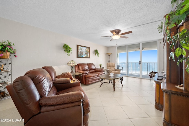 tiled living room with a water view, floor to ceiling windows, ceiling fan, and a textured ceiling