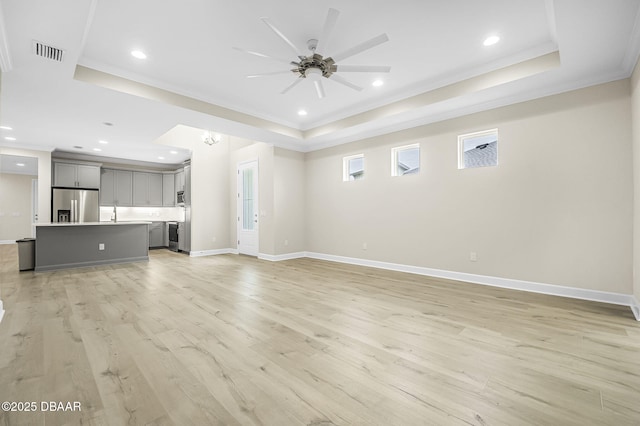 unfurnished living room with ceiling fan, light wood-type flooring, and a tray ceiling