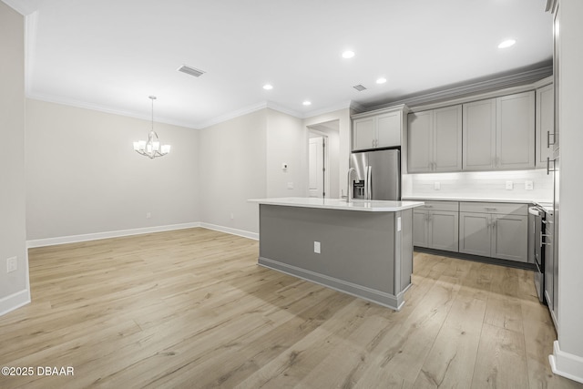 kitchen with range, a center island with sink, gray cabinetry, stainless steel fridge, and decorative light fixtures