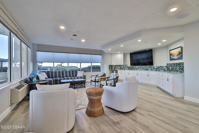 living room featuring recessed lighting, a wall mounted air conditioner, light wood-style flooring, and baseboards