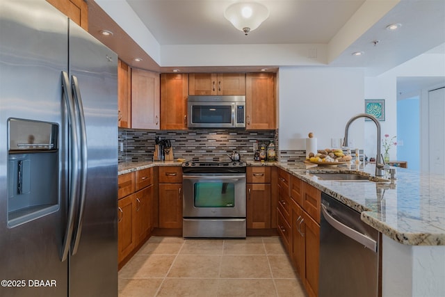 kitchen with light tile patterned floors, stainless steel appliances, brown cabinetry, a sink, and a peninsula