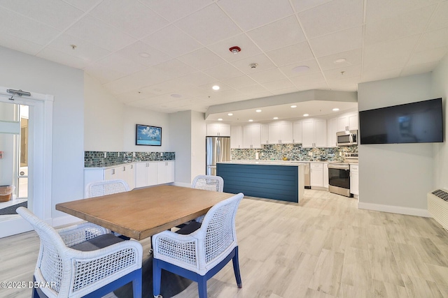 dining room with a drop ceiling, light wood-style flooring, and baseboards