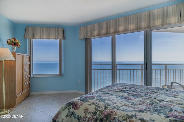 bedroom featuring a water view, light tile patterned floors, and baseboards