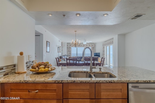 kitchen with visible vents, stainless steel dishwasher, brown cabinetry, a sink, and light stone countertops