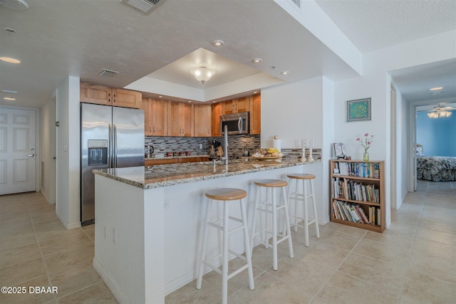 kitchen with light stone countertops, stainless steel appliances, a peninsula, visible vents, and decorative backsplash