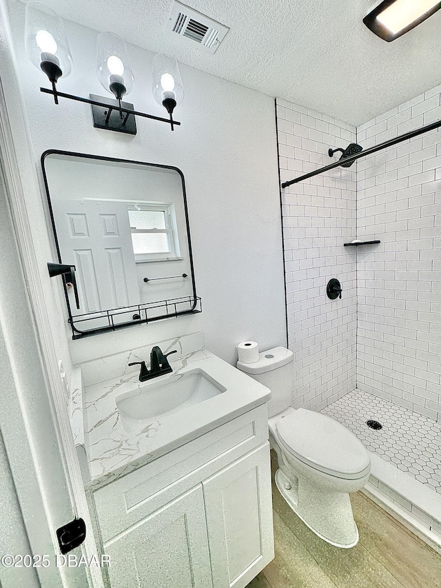 bathroom with hardwood / wood-style flooring, toilet, a textured ceiling, vanity, and tiled shower