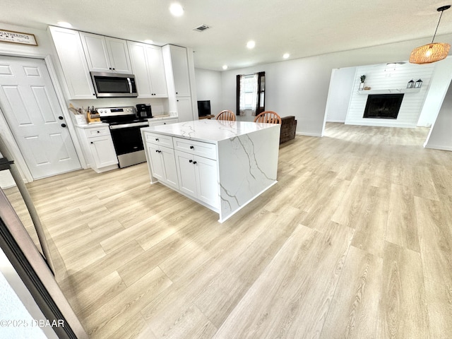 kitchen with white cabinetry, a center island, decorative light fixtures, light stone countertops, and appliances with stainless steel finishes