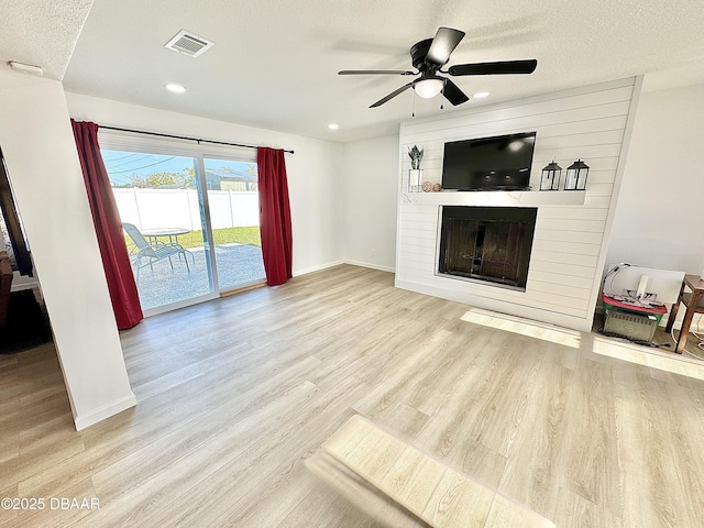 unfurnished living room featuring ceiling fan, light hardwood / wood-style flooring, a large fireplace, and a textured ceiling