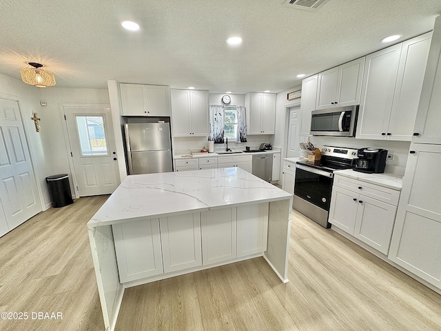 kitchen featuring stainless steel appliances, light stone counters, white cabinets, a kitchen island, and sink