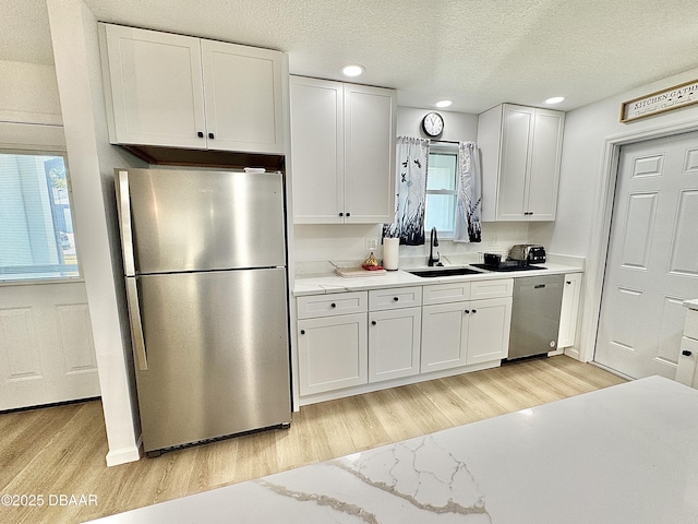 kitchen with stainless steel appliances, light stone counters, white cabinets, light hardwood / wood-style floors, and sink