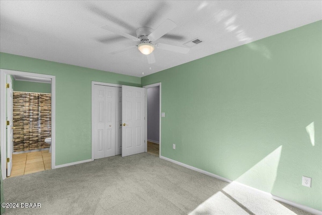 unfurnished bedroom featuring ensuite bathroom, a textured ceiling, light carpet, and ceiling fan