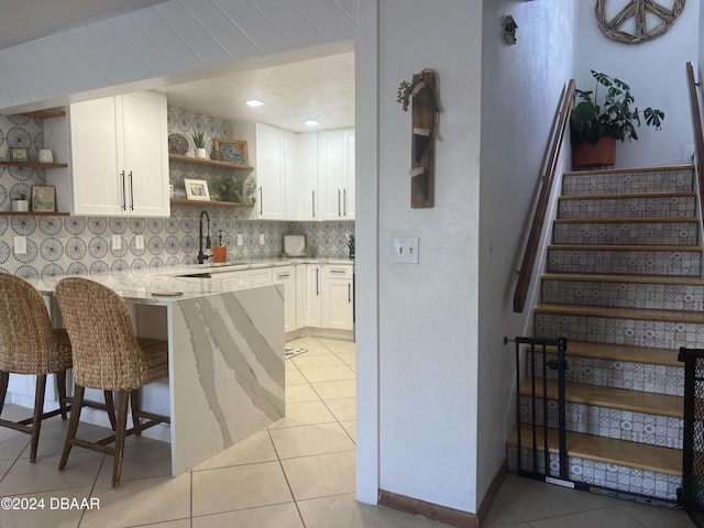 kitchen featuring light stone countertops, a kitchen breakfast bar, backsplash, sink, and white cabinetry