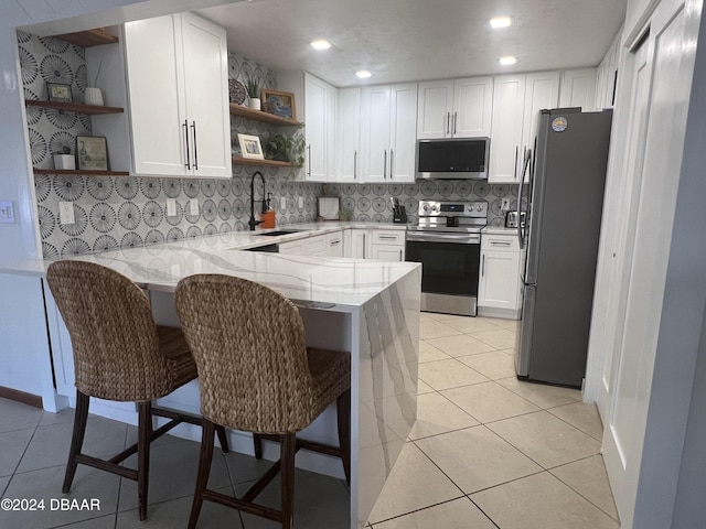 kitchen with kitchen peninsula, appliances with stainless steel finishes, white cabinets, and sink