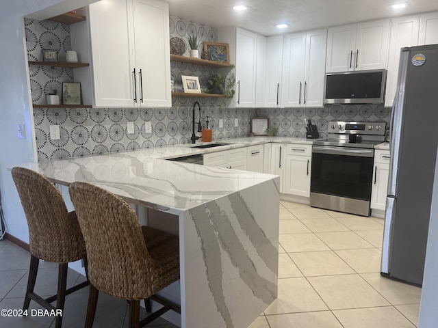 kitchen with kitchen peninsula, light stone countertops, stainless steel appliances, white cabinetry, and a breakfast bar area