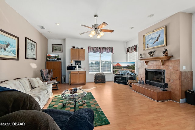 living room with ceiling fan, a fireplace, and light hardwood / wood-style floors