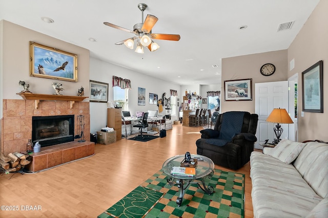 living room with ceiling fan, wood-type flooring, and a tile fireplace