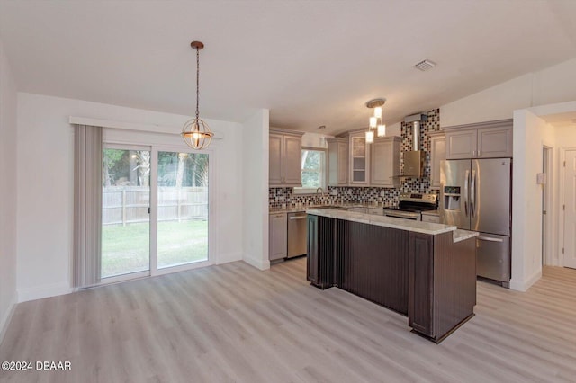 kitchen with appliances with stainless steel finishes, a healthy amount of sunlight, a kitchen island, and light hardwood / wood-style flooring