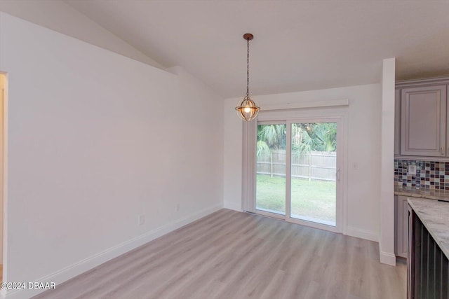 unfurnished dining area featuring vaulted ceiling and light hardwood / wood-style flooring