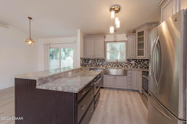 kitchen with light wood-type flooring, appliances with stainless steel finishes, decorative light fixtures, decorative backsplash, and a center island