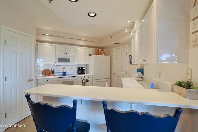 kitchen featuring kitchen peninsula, a breakfast bar area, backsplash, white appliances, and white cabinets