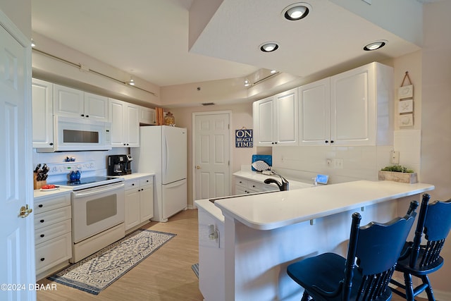 kitchen with white cabinetry, kitchen peninsula, a breakfast bar area, white appliances, and light hardwood / wood-style flooring