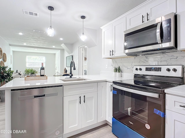 kitchen featuring sink, appliances with stainless steel finishes, decorative light fixtures, white cabinetry, and kitchen peninsula