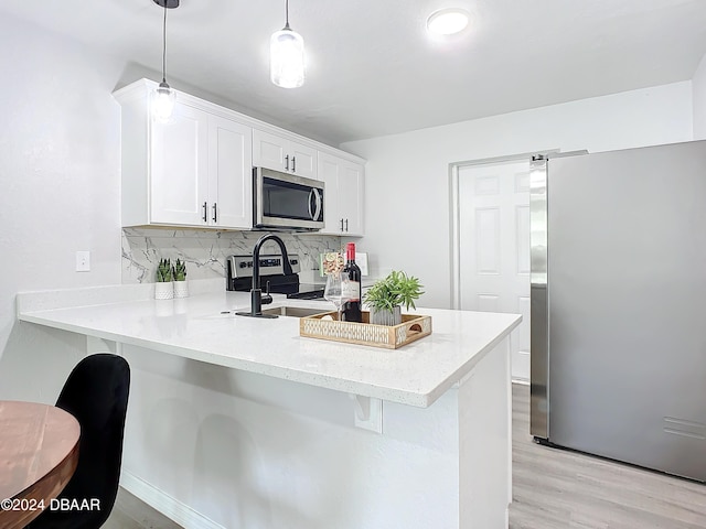 kitchen with kitchen peninsula, appliances with stainless steel finishes, light wood-type flooring, tasteful backsplash, and pendant lighting