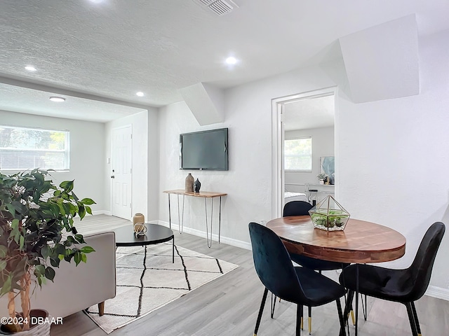 dining area with a healthy amount of sunlight, a textured ceiling, and light wood-type flooring