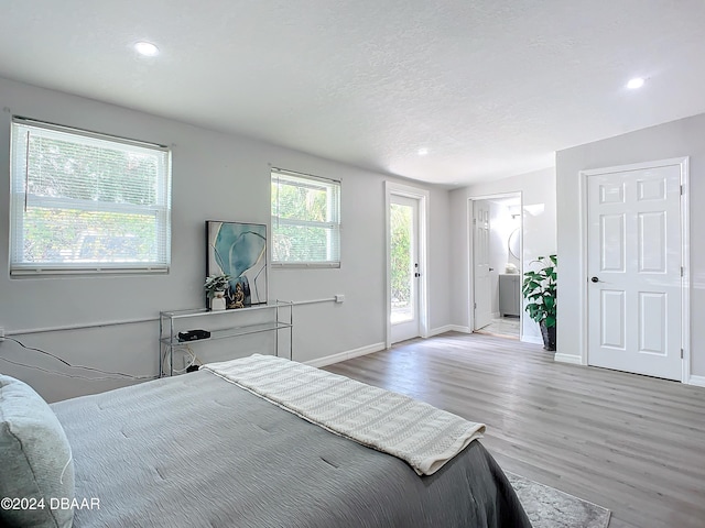 bedroom with a textured ceiling, connected bathroom, access to outside, and light hardwood / wood-style flooring