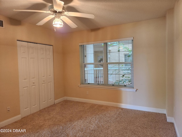 unfurnished bedroom featuring a closet, a textured ceiling, carpet flooring, and ceiling fan