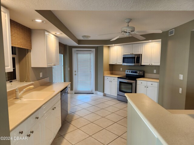 kitchen with stainless steel appliances, sink, light tile patterned floors, ceiling fan, and white cabinetry