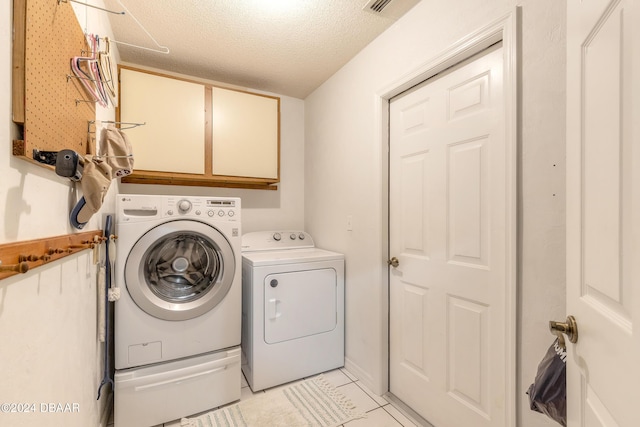 laundry area featuring cabinets, light tile patterned floors, a textured ceiling, and washer and clothes dryer