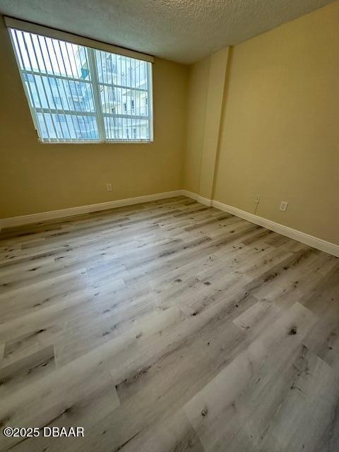 unfurnished room featuring baseboards, a textured ceiling, and wood finished floors