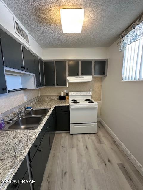 kitchen with visible vents, light wood-style flooring, under cabinet range hood, a sink, and white range with electric stovetop