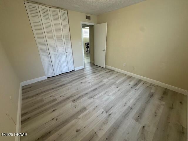 unfurnished bedroom with light wood-style floors, visible vents, a closet, and a textured ceiling