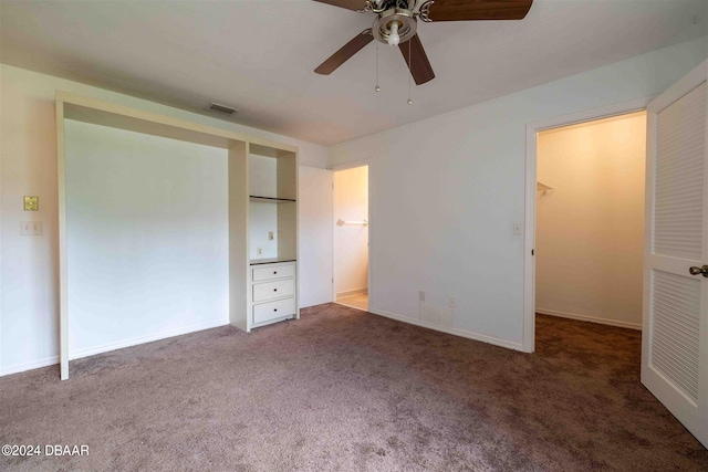 unfurnished bedroom featuring dark colored carpet, ceiling fan, a walk in closet, and a closet