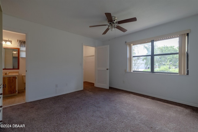 unfurnished bedroom with ensuite bathroom, ceiling fan, a walk in closet, a closet, and carpet floors