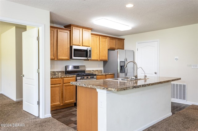 kitchen featuring a kitchen island with sink, stainless steel appliances, a textured ceiling, and sink