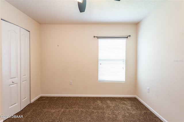 unfurnished bedroom with a textured ceiling, a closet, ceiling fan, and dark carpet