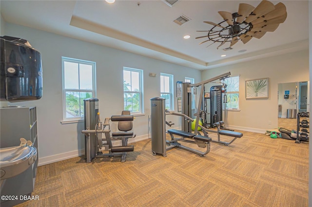 exercise area featuring light carpet, ceiling fan, and a raised ceiling